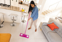Biracial Young Woman Cleaning Floor In Living Room With Mop At Home