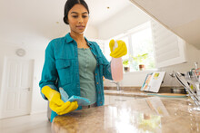 Biracial Young Woman Wearing Gloves Cleaning Kitchen Counter At Home