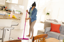 Biracial Young Woman Cleaning Tiled Floor In Living Room With Mop At Home