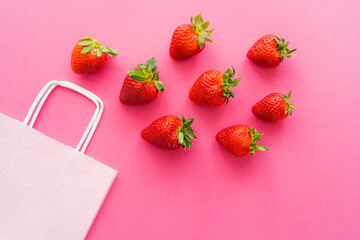 Wall Mural - Top view of fresh strawberries with leaves near shopping bag on pink background.
