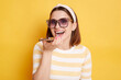 © sementsova321 - Indoor shot of satisfied happy adorable young woman wearing striped t-shirt posing isolated over yellow background, using cell phone for recording voice message.