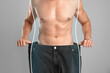 © New Africa - Closeup view of man with slim body in oversized jeans on grey background. Weight loss