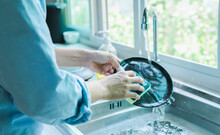 Close-up Of A Woman Washing Dishes With Dirty Food Scraps Cleaner In The Sink The Kitchen Counter At Home.