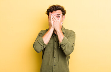 Wall Mural - young handsome man covering face with hands, peeking between fingers with surprised expression and looking to the side