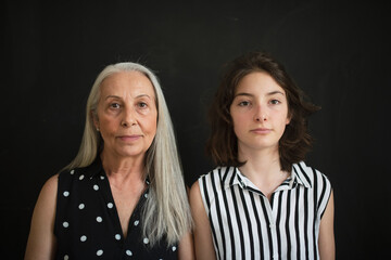 Wall Mural - Portrait of senior grandmother with her granddaughter looking at camera over black blackground