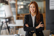 Cheerful asian businesswoman entrepreneur smiling at the camera while standing with her arms crossed. Happy young businesswoman standing in the boardroom of a modern workplace.