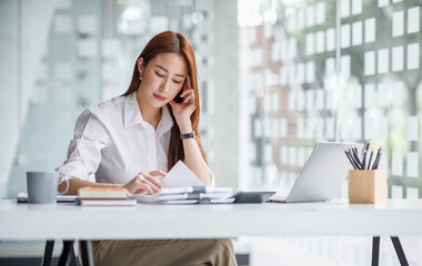 Portrait of happy young Asian woman celebrating success with arms up in front of a laptop at office