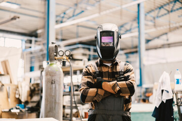 Wall Mural - A metallurgy worker with protective welding mask on face standing in facility.