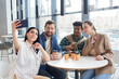 © Seventyfour - Group of diverse adult people taking selfie photo while sitting at table in cafe indoors