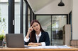 © Natee Meepian - Asian woman sitting at desk near computer cogitating thinking making important decision at workplace. Concentrated serious office worker millennial woman analysing results feels doubts and feel unsure