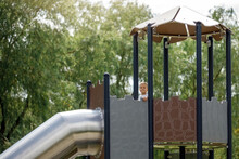 A little boy in the high observation tower of the playground prepares to slide through a metal tunnel.