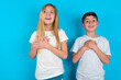 © Jihan - Happy smiling two kids boy and girl standing over blue studio background has hands on chest near heart. Human emotions, real feelings and facial expression concept.