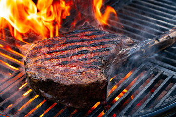 Barbecue dry aged wagyu tomahawk steak offered as close-up on a charcoal grill with fire and smoke