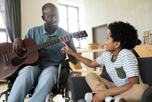 Little Son Pointing At Strings On Guitar While His Disabled Father Playing Music For Him During Their Leisure Time At Home