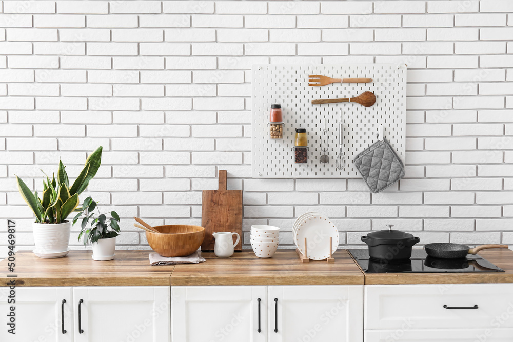 Counters with kitchen utensils, stove and houseplants near white brick wall