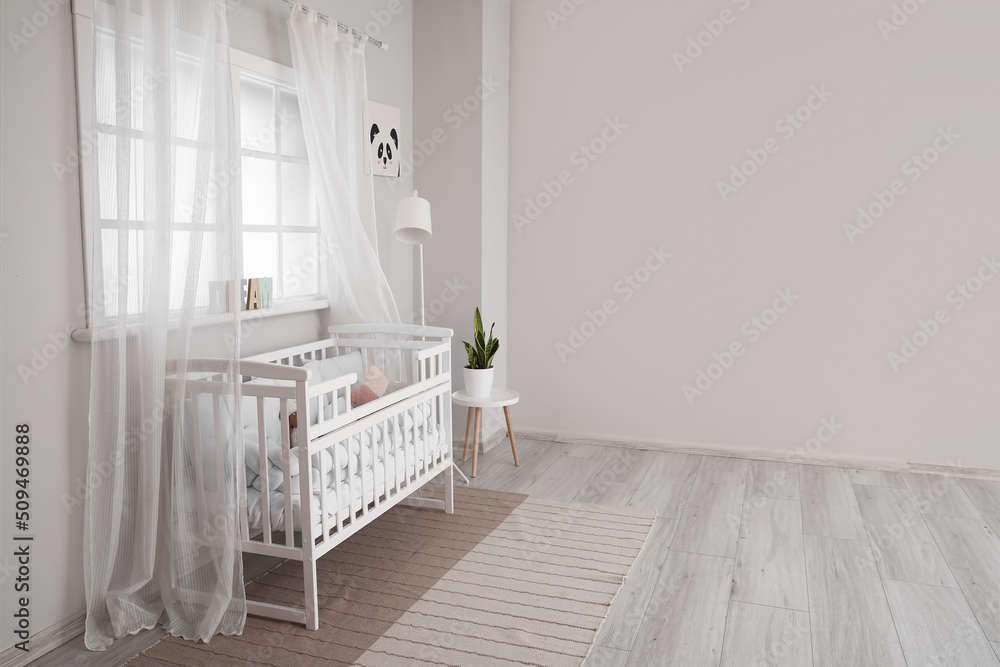 Interior of light nursery with baby crib, lamp and window