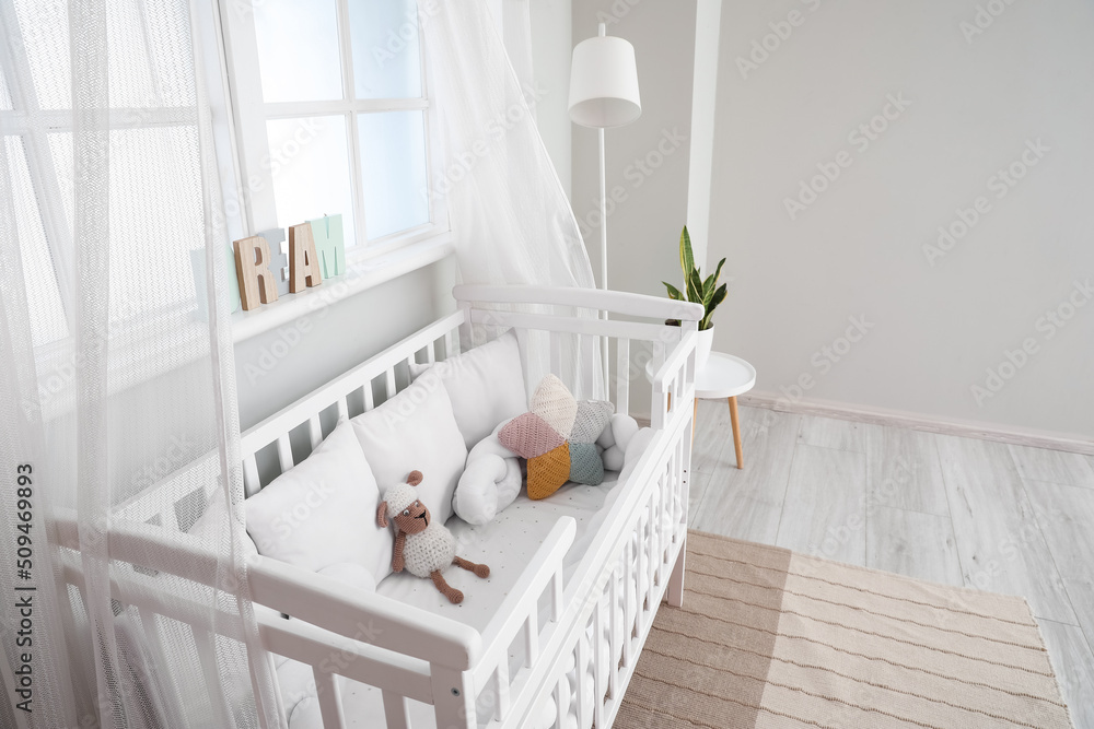 Interior of light nursery with baby crib, lamp and window
