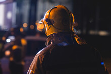 Group Of Fire Men In Uniform During Fire Fighting Operation In The Night City Streets, Firefighters With The Fire Engine Truck Fighting Vehicle In The Background, Emergency And Rescue