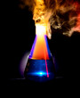 Strong chemical reaction with a lot smoke and vapors inside Erlenmeyer flask. Ignition is starting. Vessel with a blue liquid is standing on the table. 
