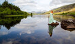 Lady of the lake with a sword and standing on a rock is reflected in a still lake surrounded by mountains; Llyn Mymbyr Capel Curig Wales 