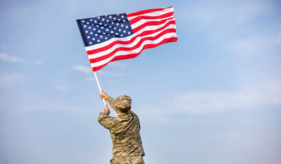 Male soldier in the uniform of the American army waving the US flag on top of a mountain in a clearing at sunset