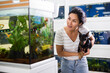 Asian woman with dog in hands looking at aquarium in pet shop.