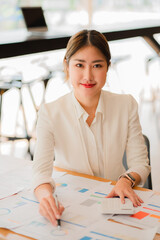 Asian businesswoman analyzing a report pointing to a graph with a pen, laptop, and calculator. In the online marketing concept of workstation accountant's vertical e-commerce landscape