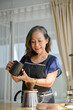 © bongkarn - Beautiful Asian retired woman pouring a hot water into a drip coffee bag and drip kettle