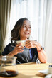 © bongkarn - Happy relaxed mature older adult woman drinking coffee in living room.