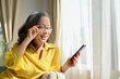 © bongkarn - Happy asian retired woman in glasses relaxes, using modern mobile phone