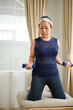 © bongkarn - Portrait of an active asian aged woman focused exercising, lifting dumbbells