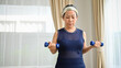 © bongkarn - Healthy Asian senior aged woman doing exercise at home, lifting a small dumbbells.
