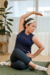 © bongkarn - Healthy asian aged woman sits on yoga mat and stretching her arms and legs.