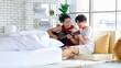 © Bangkok Click Studio - Two Asian young happy romantic lovely teenager male gay men lover couple partner sitting smiling on cozy sofa in bedroom cuddling hugging together while husband playing acoustic guitar and sing song