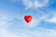 Heart-shaped chocolate bonbon wrapped in red foil on a blue background with white clouds