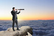  businessman with telescope standing on cliff and looking into the distance on bright blue sky and clouds background with mock up place for your advertisement. 