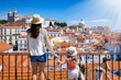 Leinwandbild Motiv A tourist mother and her daughter on family holidays look at the beautiful cityscape of Lisbon, with the colorful houses and roofs at the Alfama district, Portugal