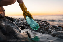 Earth Day. Volunteer In Protective Gloves Picks Up A Plastic Bottle On The Beach. Close Up Of Hand. Low Angle View. Copy Space. The Concept Of Cleaning The Coastal Zone