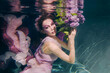 woman with lilac bouquet in colorful clothes on the dark background swimming underwater 