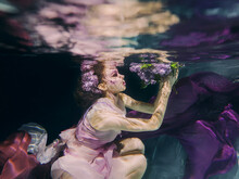 Woman With Lilac Bouquet In Colorful Clothes On The Dark Background Swimming Underwater 