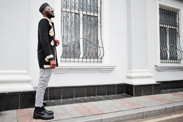 Wall Mural - Mega stylish african man in traditional jacket pose. Fashionable black guy in hat and sunglasses with cigar in hand.