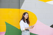Young woman standing near bright colorful wall using mobile phone, video chatting or calling or texting using social media. Happy lifestyle candid moments of life