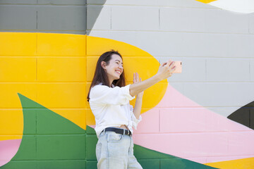 Young woman standing near bright colorful wall using mobile phone, video chatting or calling or texting using social media. Happy lifestyle candid moments of life