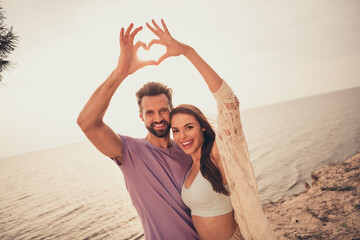 Canvas Print - Portrait of two attractive cheerful people spending honey moon hugging showing heart symbol at beach outdoors