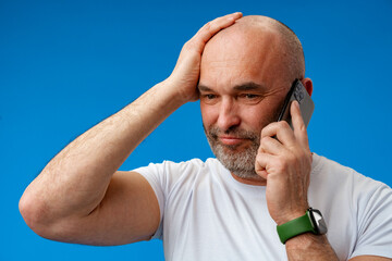 Wall Mural - Portrait of an adult man talking on the phone against blue background.