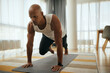© Drazen - Young African American athletic man in plank pose doing running abs exercise during home workout.