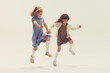 © Lustre Art Group  - Portrait of two cheerful happy girls, children in beautiful dresses playing together, jumping isolated over grey studio background