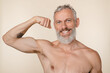 © InsideCreativeHouse - Strong caucasian mature middle-aged man shirtless with bare shoulders showing his power muscles male strength , showing his tattoo looking at camera isolated in beige background