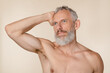 © InsideCreativeHouse - Caucasian strong middle-aged mature man with grey hair and beard and muscles shirtless with bare shoulders isolated in beige background. Male beauty concept