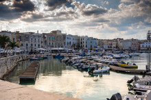 Trani, Puglia, Italy. August 2021. Beautiful View Of The Marina Surrounded By Houses With Colored Facades, Dramatic Sky With Rays Of Light Filtering Through The Clouds.